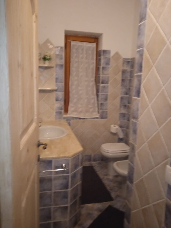 Un baño pequeño con lavamanos, inodoro y ventana, con una toalla colgada.