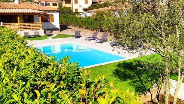 Zona de piscina con sillones de descanso, cielo azul despejado y follaje circundante.