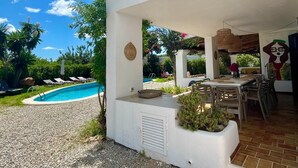 Ein Poolbereich mit überdachter Terrasse, Sitzgelegenheiten im Freien und Blick auf ein Schwimmbecken.