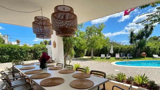 Ein Essbereich im Freien mit Pool, Korbstühlen und einem Tisch mit Untersetzern.