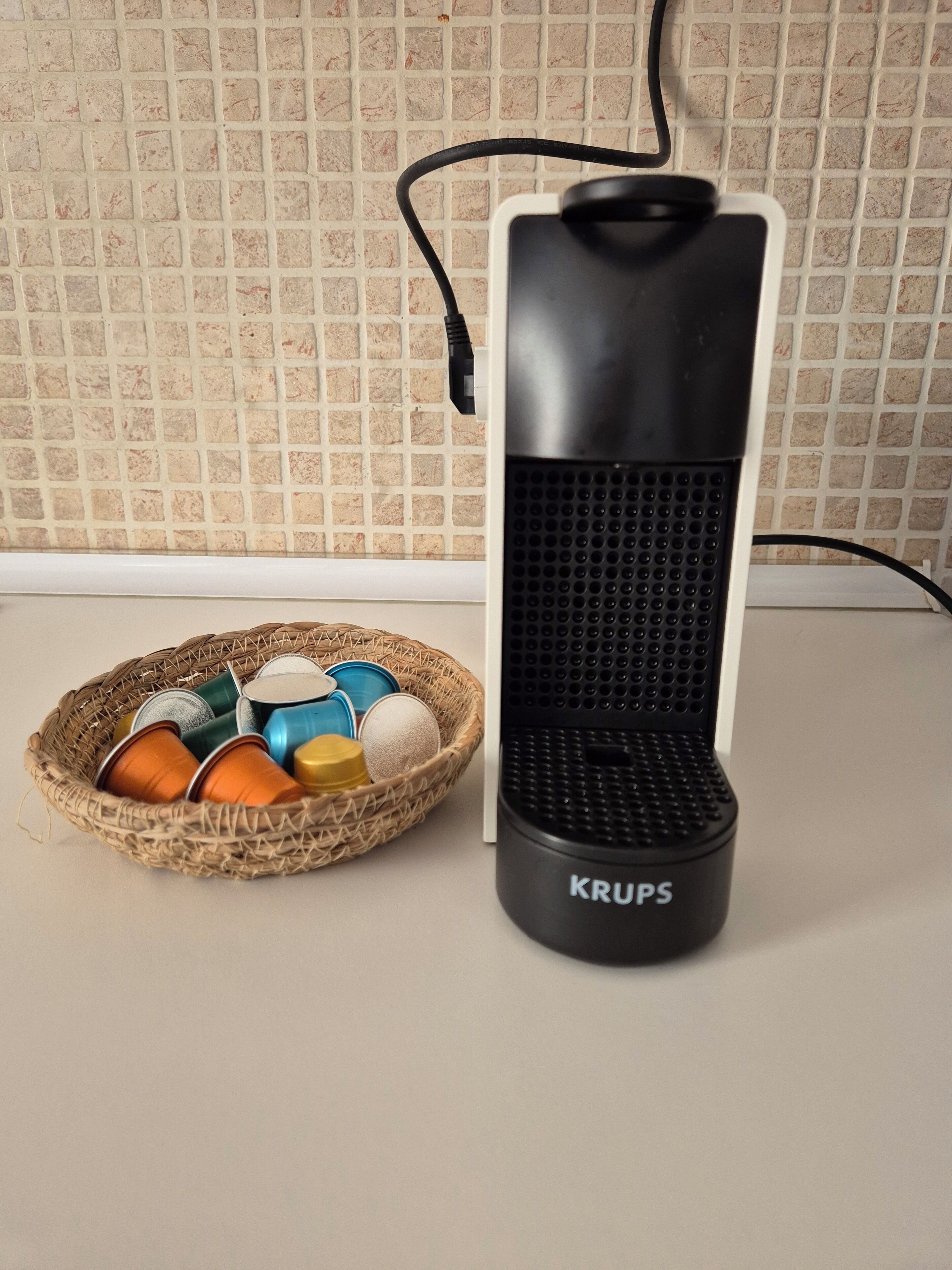 Ein schwarzer Krups Wasserkocher mit einem Korb voller bunter Blechdosen daneben.
