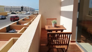 Ein Balkon mit Holztisch und -stühlen, einem Blumentopf und Blick auf einen Parkplatz mit Autos.