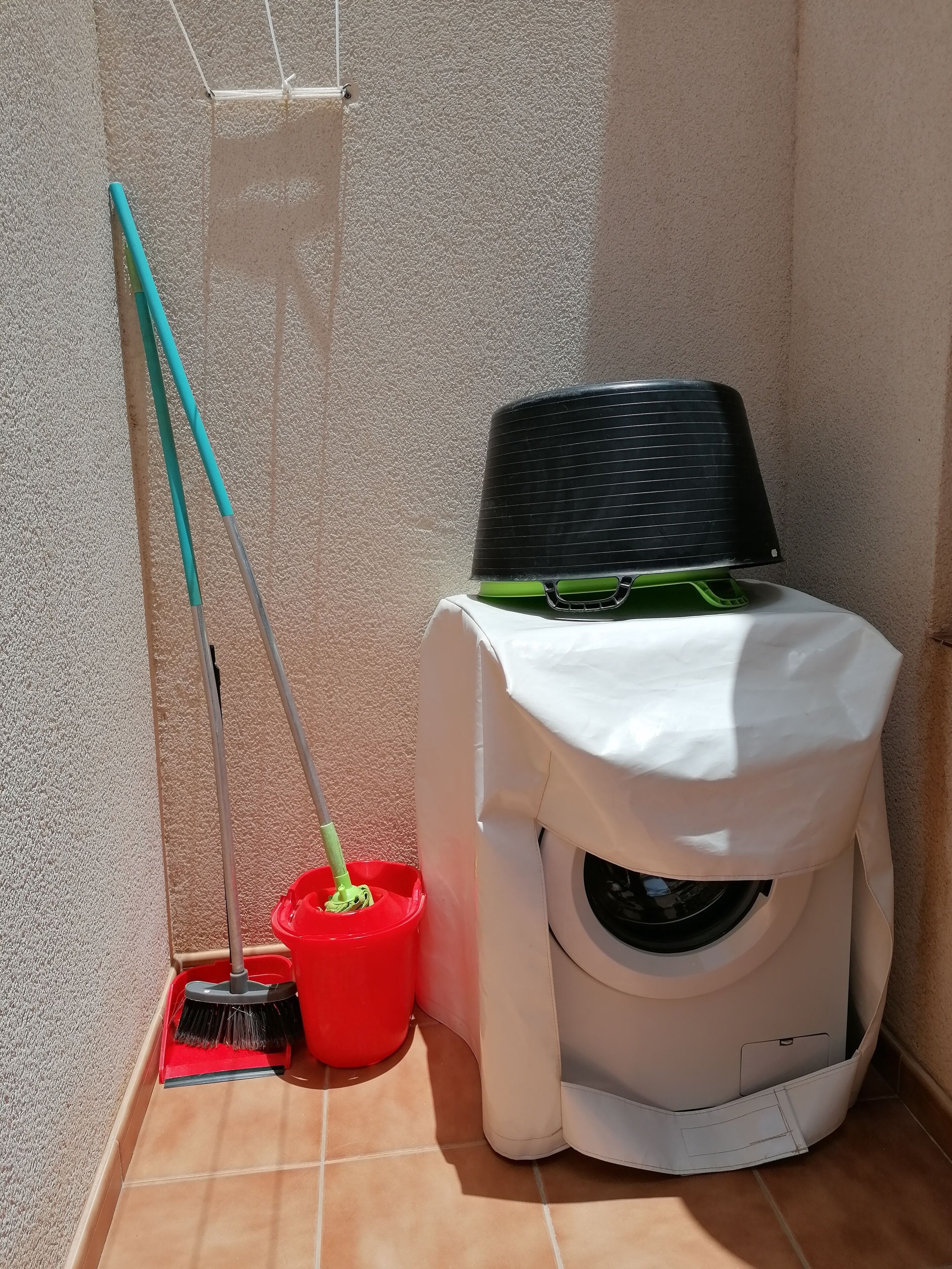 A compact, white, wall-mounted toilet with a green seat and a black lid. Adjacent to it is a red bucket with a broom and dustpan.