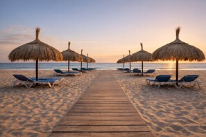 A wooden pathway leading to beach umbrellas and lounge chairs on a sandy beach.