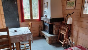 L’intérieur chaleureux d’un chalet avec une table et des chaises en bois, une cheminée et un lit recouvert d’une couverture rouge et blanche.