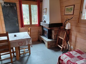 A cozy cabin interior with a wooden table and chairs, a fireplace, and a bed with a red and white quilt.