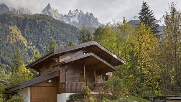 Une cabane en bois dotée d’un balcon, entourée d’arbres et avec des montagnes en arrière-plan.