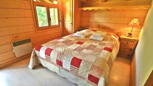 Une chambre dans une cabane en bois, avec une couvre-lit matelassé, une table de chevet avec une lampe et une fenêtre donnant sur un paysage verdoyant.