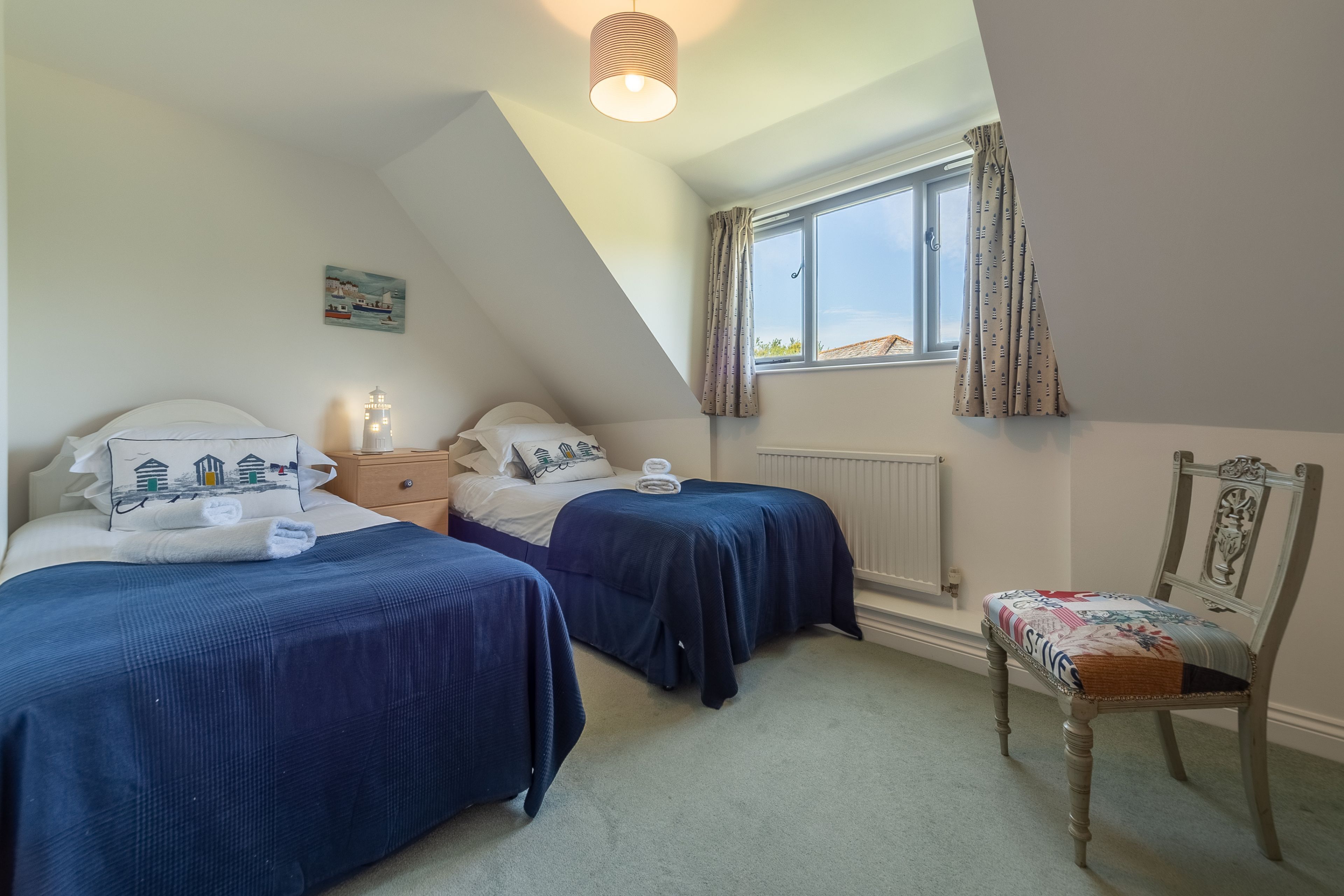 A bedroom with two beds, a window with curtains, a radiator, and a chair with a floral cushion.