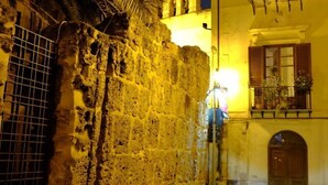 Une rue étroite, bordée d’un côté par un mur de pierre et de l’autre par un immeuble doté d’un balcon.