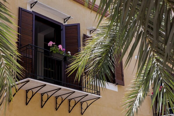 Un balcon orné d’une balustrade en fer forgé et d’un pot de fleurs contenant des fleurs roses.