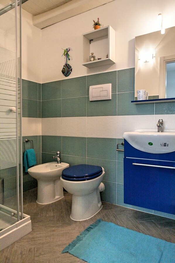 Un baño con cabina de ducha de vidrio, un lavamanos blanco, un inodoro azul y un mueble de tocador azul.