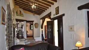 A cozy living room with a stone wall, a black leather sofa, and a wooden ceiling. - Finca Carrulo with private pool for 6 people and fantastic views (Cómpeta)