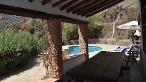A covered outdoor area with a pool, stone pillars, and lounge chairs. - Finca Carrulo with private pool for 6 people and fantastic views (Cómpeta)