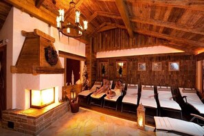 A rustic room with a stone fireplace, wooden beams, and multiple sun loungers. - Vitalhotel Tauernhof (Grossarl)