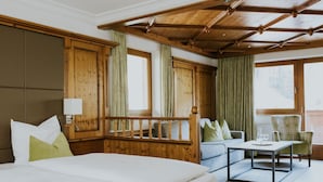Habitación de hotel con cama, sofá, mesa y una silla. Hay cortinas y paneles de madera en las paredes.
