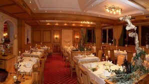 A formal dining room with multiple tables set for service, wooden paneling, and a chandelier. - Vitalhotel Tauernhof (Grossarl)