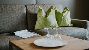 A modern living room with a grey sofa, green cushions, a wooden coffee table, and a pair of glasses on a magazine. - Vitalhotel Tauernhof (Grossarl)