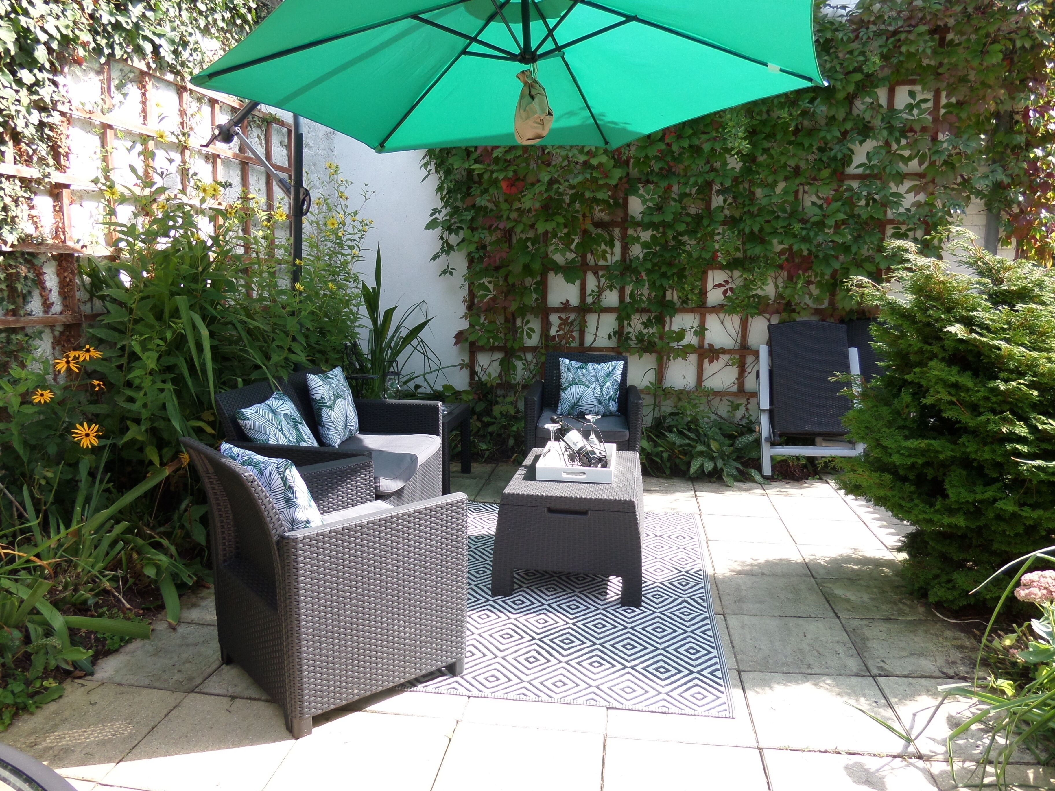 A patio area with wicker furniture, a patterned rug, and a green umbrella.