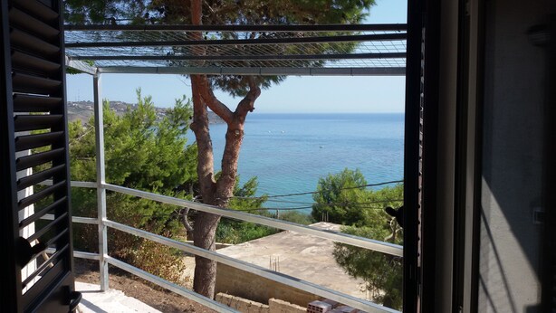 Un balcon avec vue sur la mer, un arbre et un ciel dégagé.