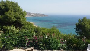 Un paysage côtier offrant une vue sur la mer, la verdure et une côte lointaine parsemée de bâtiments.