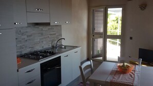 Une cuisine moderne équipée d’une cuisinière à gaz, d’un évier et d’un lave-vaisselle, ainsi qu’une table à manger avec des chaises et une porte-fenêtre coulissante donnant sur un balcon.