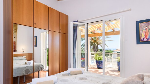 A bedroom with a large bed, wooden wardrobe, and a sliding glass door leading to a balcony with outdoor furniture. - IDEAL LARGE FAMILIES, facing the sea and a few meters from the beach of Binibeca (Binibequer)