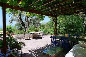 Un patio al aire libre con una pérgola, suelo de piedra y una mesa con sillas.