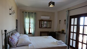 Un lit bien fait, avec du linge de lit blanc, une table de chevet, un luminaire suspendu, une fenêtre avec des rideaux et une porte avec des panneaux de verre.