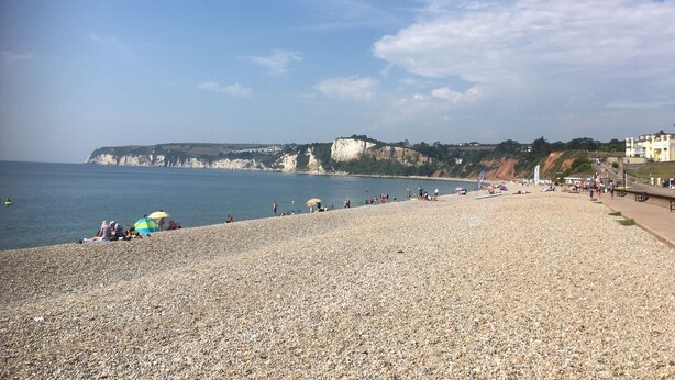 A pebbled beach with people, umbrellas, and cliffs in the background. - DAISY COTTAGE in peaceful rural location (Colyton)