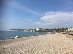 A pebbled beach with people, umbrellas, and cliffs in the background. - DAISY COTTAGE in peaceful rural location (Colyton)
