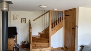 A wooden staircase with a handrail, a black fireplace, and a television on a wooden stand. - DAISY COTTAGE in peaceful rural location (Colyton)