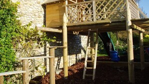 A wooden play structure with a slide and climbing elements, set against a stone wall. - DAISY COTTAGE in peaceful rural location (Colyton)