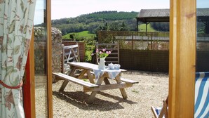 A wooden picnic table with a white tablecloth and a vase of flowers, set on gravel with a view of green hills. - DAISY COTTAGE in peaceful rural location (Colyton)