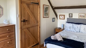 A bedroom with a wooden wardrobe, a bedside table with a lamp, a bed with a blue blanket, and a framed picture on the wall. - DAISY COTTAGE in peaceful rural location (Colyton)
