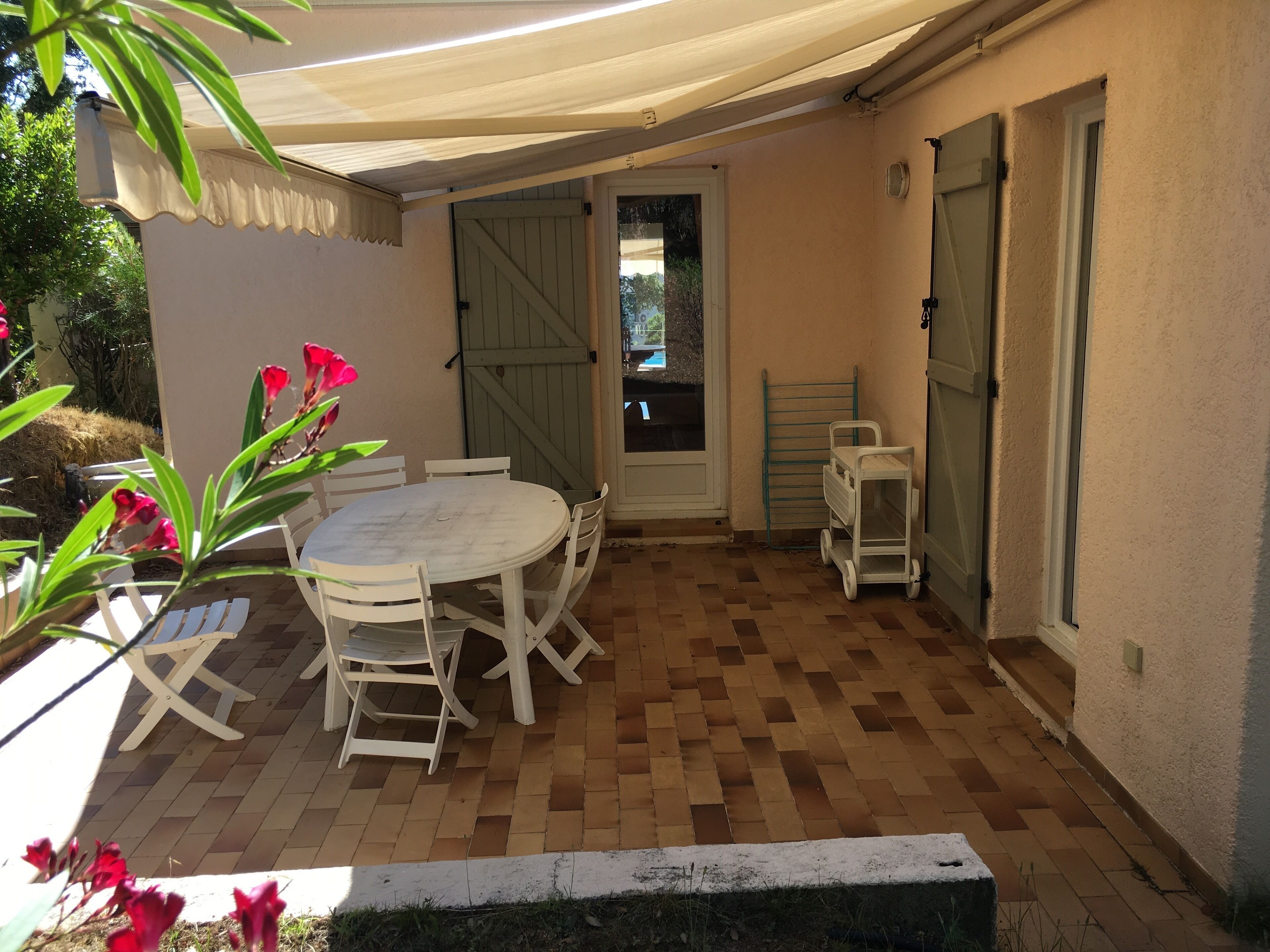 Un patio al aire libre con una mesa redonda y sillas, una pared blanca y una puerta que da al exterior.