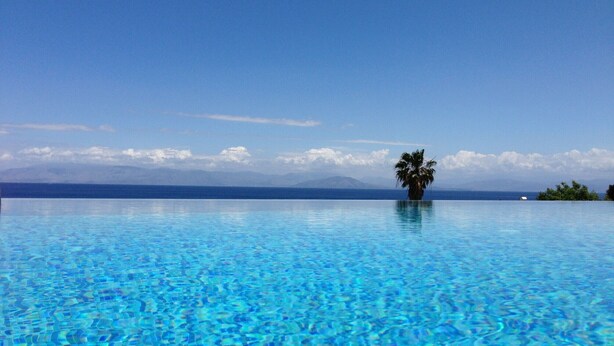Une magnifique piscine à débordement d’un bleu profond, avec un palmier au centre, le tout entouré d’un paysage montagneux.