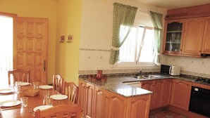Una cocina con armarios de madera, una mesa de comedor lista para cuatro personas y un ventanal con cortinas.