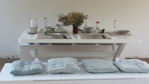 Una mesa de comedor dispuesta con platos, tazones, vasos y un jarrón con flores.