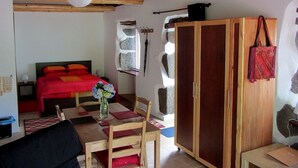 Ein Zimmer mit einem Bett, einem Holztisch mit Stühlen, einem Schrank aus Holz und einer aufhängbaren Tasche.