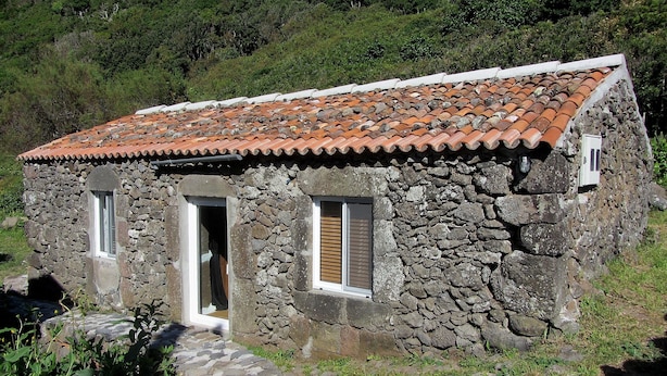 Ein Haus aus Stein mit Ziegeldach, einer Holztür und einem Fenster mit Rollläden.