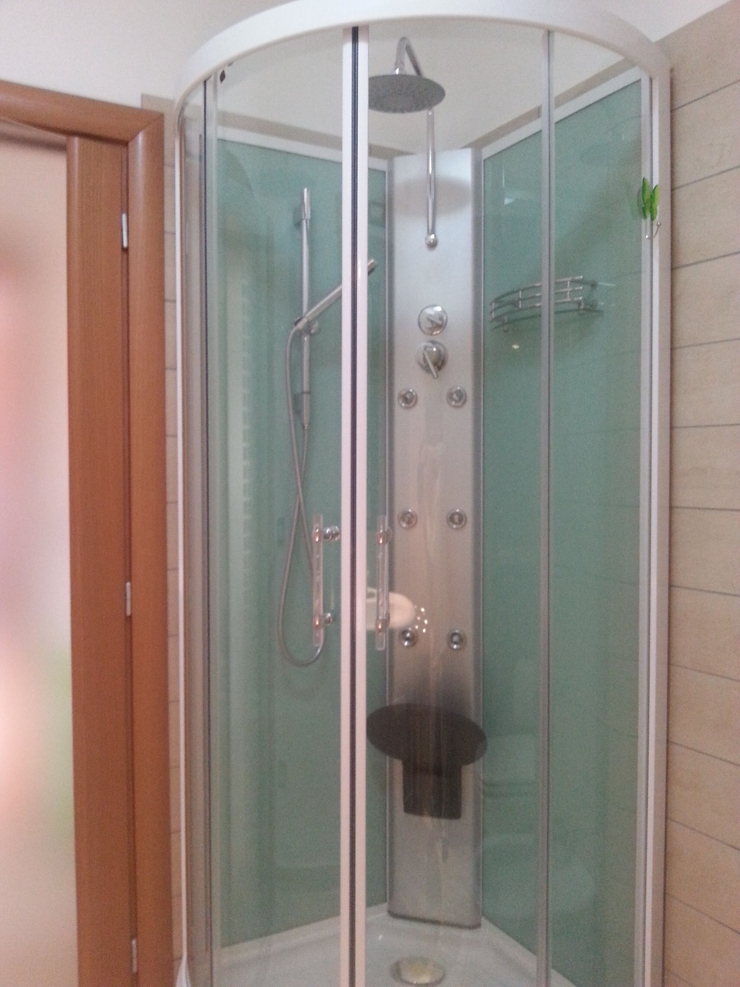 Eine Duschkabine mit Glaswänden, einer Handbrause und einem am Wand montierten Wasserhahn.