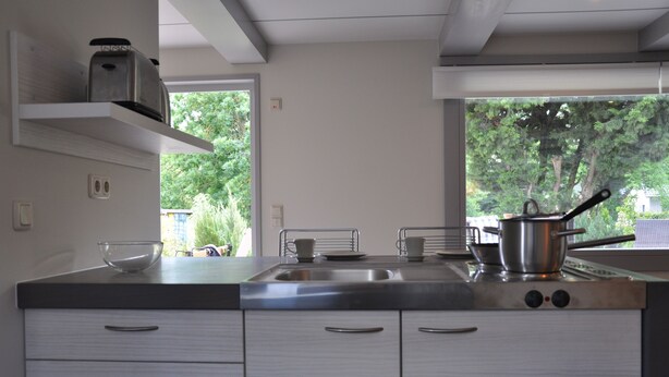A modern kitchen with stainless steel appliances, white cabinetry, and a view of greenery outside.
