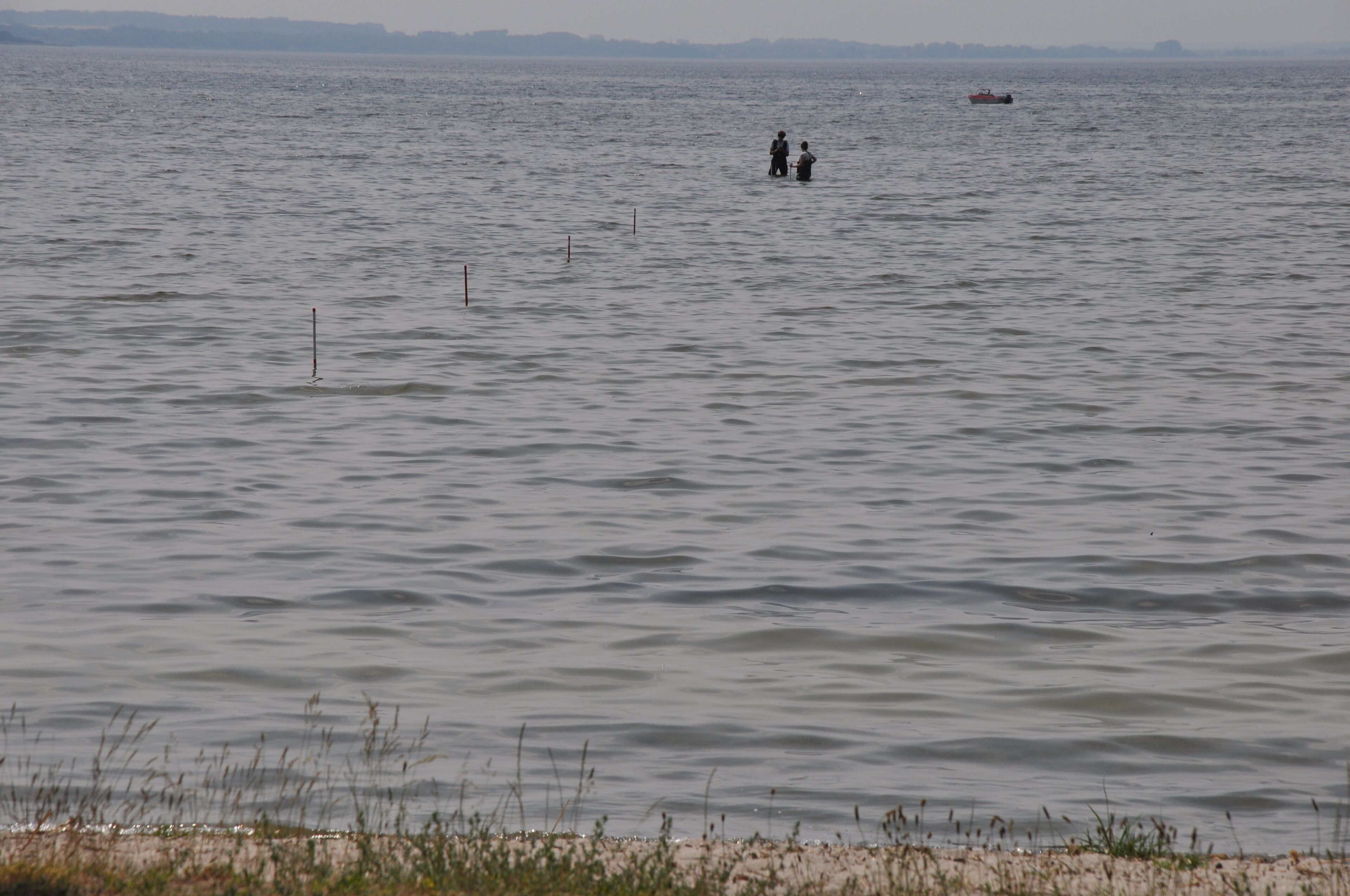 A calm body of water with two people standing in the distance.