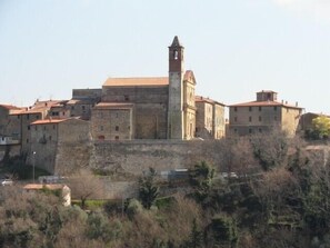 Un bâtiment historique en pierre, doté d’une tour imposante, entouré d’autres bâtiments aux toits recouverts de tuiles rouges.