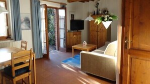 Een gezellige woonkamer met een houten plafond, een bank, een televisie en een eethoek met een tafel en stoelen.