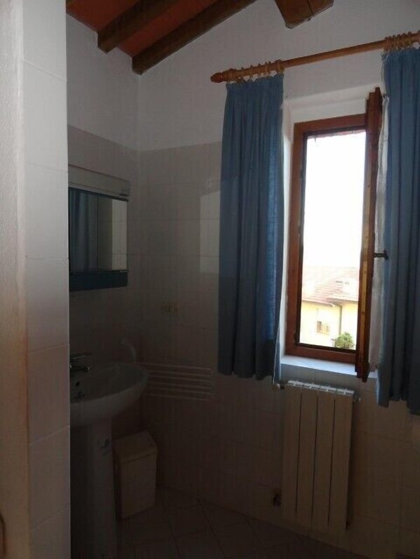 A small bathroom with a sink, a mirror, a window with curtains, and a radiator. - Beautiful stone house in Tuscany with terrace and balcony. (Caldana)