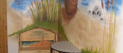 Una habitación con un mural al estilo playero, una cama de madera y una mesita.