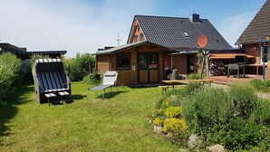 A wooden house with a tiled roof, a barbecue area, and two outdoor seating areas. - Family apartment with sea view (Fehmarn)