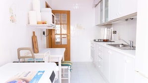 Een compacte keuken met witte kastjes, een houten deur en een klein eethoekje met een tafel en stoelen.
